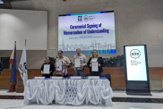 BGS staff stand with PHIVOLCS staff behind a desk. They each hold a signed MoU document. 