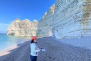 Dr Carole Nehme, examining the chalk cliffs at Étretat. She wears a hard hat. The sea is behind her.