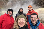 Five BGS staff members standing in front of a hot spring. All are in jackets and hats. 