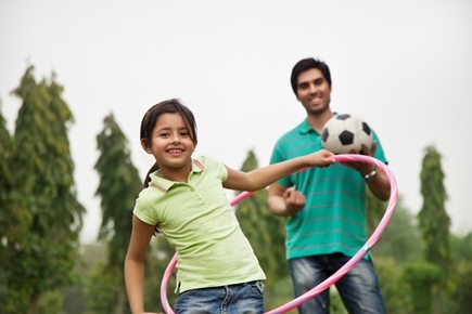 young girl playing with a hoola hoop with a man stood behind her