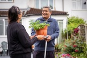 Photograph of man and women chatting and passing a plant pot between them