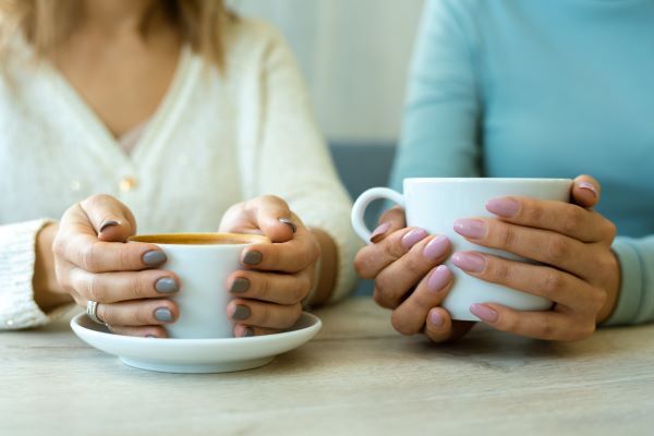 Photo of two women's hands holding cups of tea