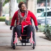 Photo of lady in a wheelchair wheeling herself along a pavement