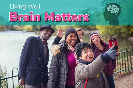 Group of five friends, various races and genders aged 45 - 65, taking a selfies next to lake dressed in hats and coats