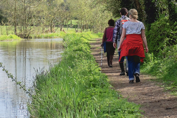 three people walking away from camera along a canal tow path