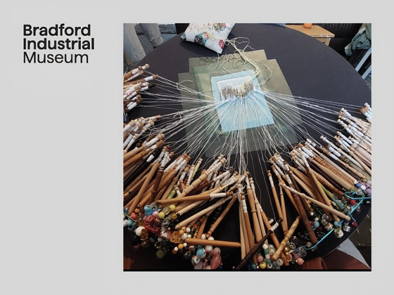 Bobbin lace setup with multiple wooden bobbins and threads arranged around a lace pattern.