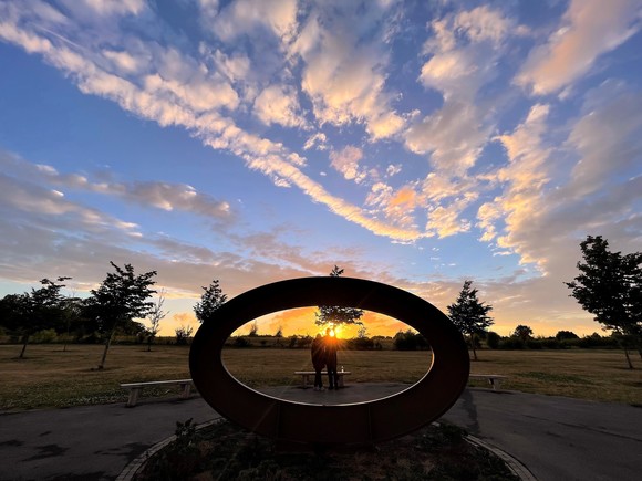 A couple posing behind an oval sculpture at Cabbage Hill, at dusk
