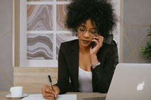 Lady on the her phone with her laptop and pad of paper in front of her