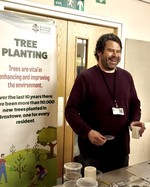 Man holding cup of tea infront of tree planting poster. Green festival