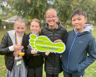 Children holding a sign 'taking action to reduce our carbon footprint'