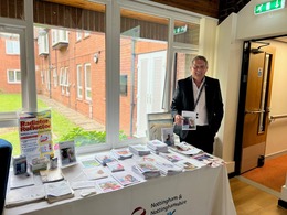 age uk employee standing next to table with lots of flyers on support for scam and other areas