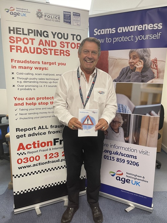Age UK Nottingham staff member standing holding scam prevention 