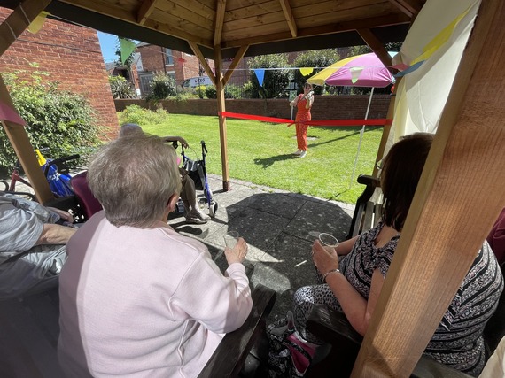 women playing violin to tenants under a wooden gazebo in the sunshine