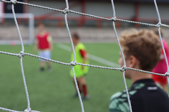 Four young football players on a field seen through a football goal net