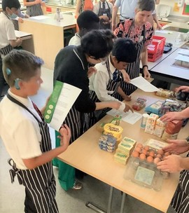 2 adults and two children in aprons standing around a table looking at ingredients