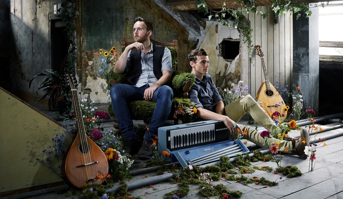 A photograph of two men with musical instruments surrounded by flowers