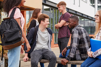 Photo of young people outside a school. Two boys are sitting on a bench talking to each other