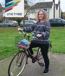 a woman on her bike with a pile of books in the front basket.  Logo reads “Love to Ride”