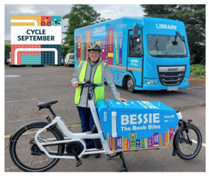 A librarian wearing a helmet and a Hi Vis vest, holding Bessie the book bike in front of a mobile library
