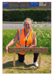 Woman wearing a high-vis vest smiling behind a sign in a field