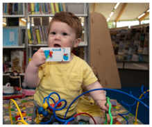 Toddler holding a library card paying in a library