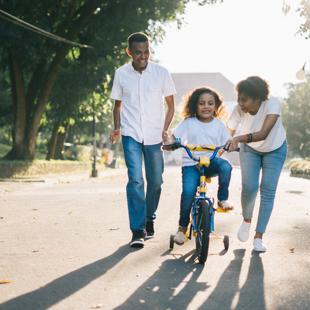 Two adults helping a young child to ride a bicycle 