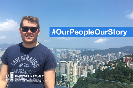 A man standing in front of a coastline with skyscrapers and text #OurPeopleOurStory