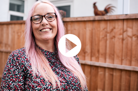 Louise smiling in garden with 'play' symbol. 