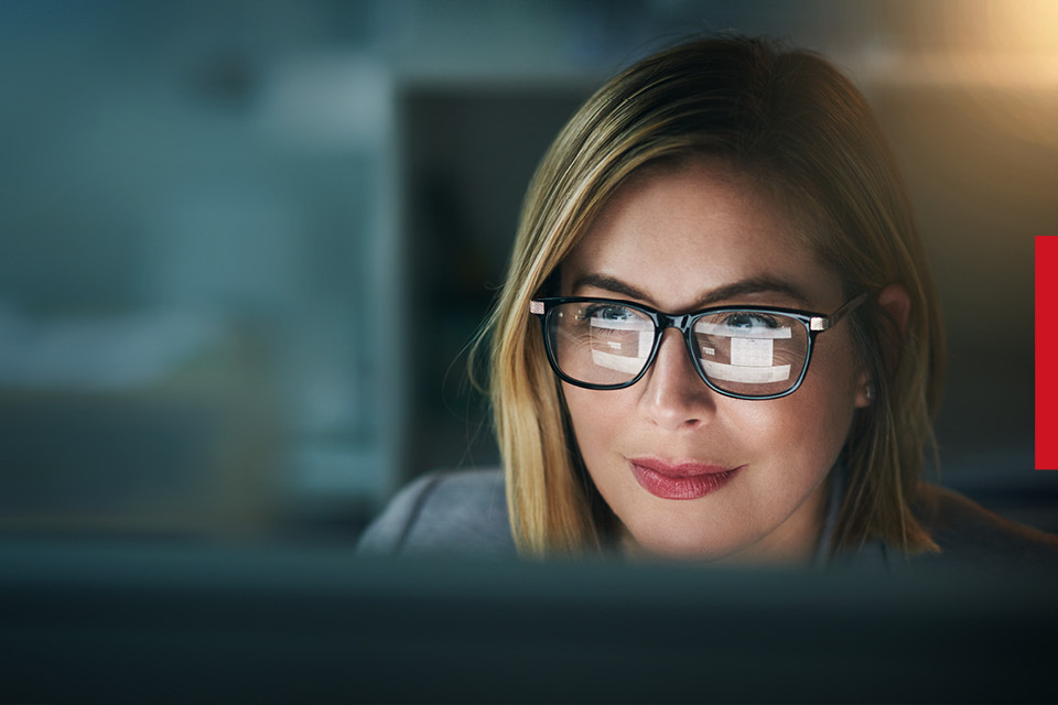 A woman working at a computer with the screen reflecting in her glasses. 