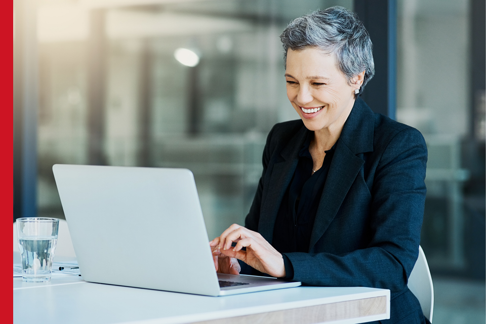 A smartly dressed woman smiles whilst using her laptop