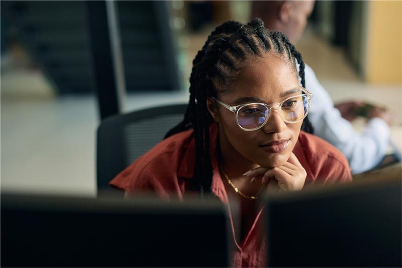 A young woman in glasses is looking at a computer screen