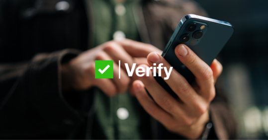 Two hands holding and typing on a mobile phone, the word verify is overlaid with a green tick 