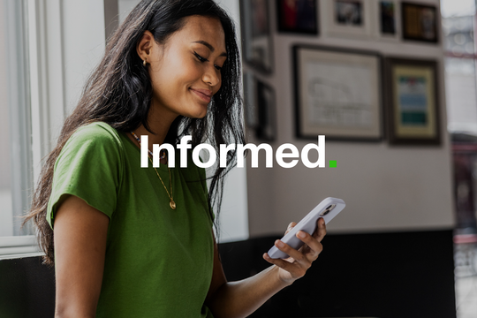 A woman in a green jumper is smiling whilst typing on her smart phone