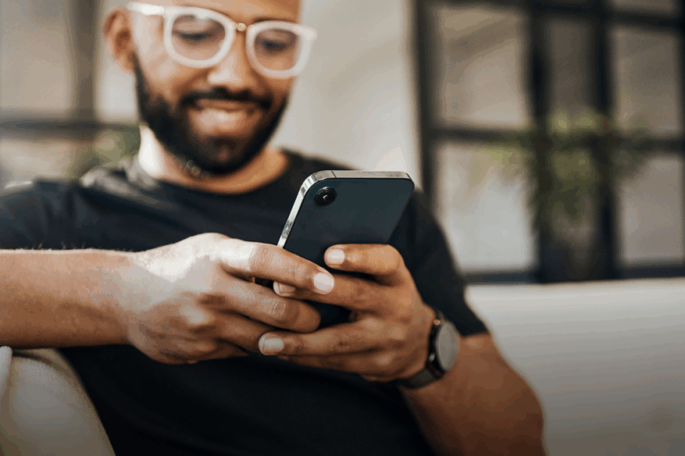 A man smiles whilst typing on his mobile phone