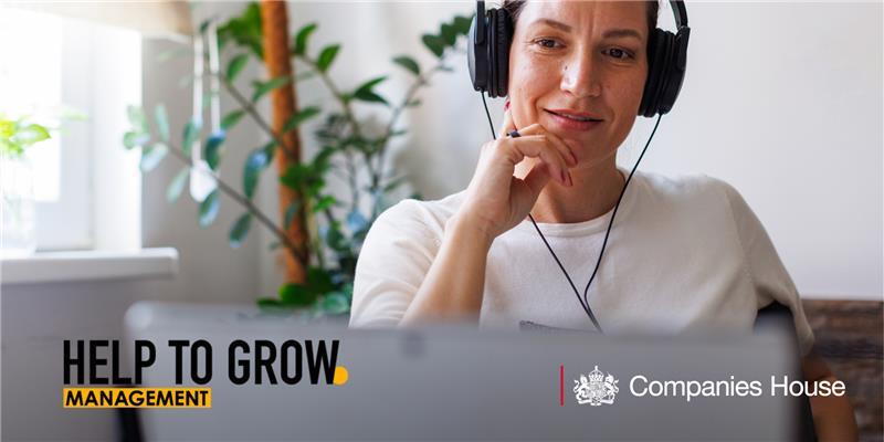 A woman wearing headphones smiles looking at her laptop