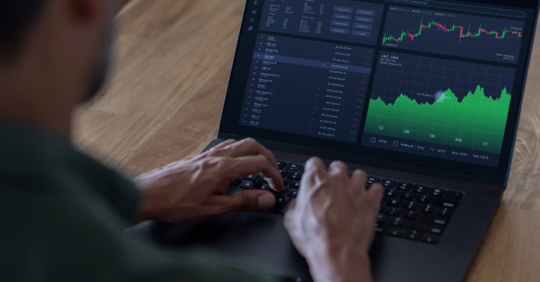 Hands typing on the keyboard of a laptop with data and graphs on the screen