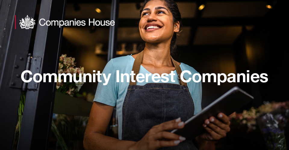 A woman is smiling, stood in a florist with a tablet device in her hand 