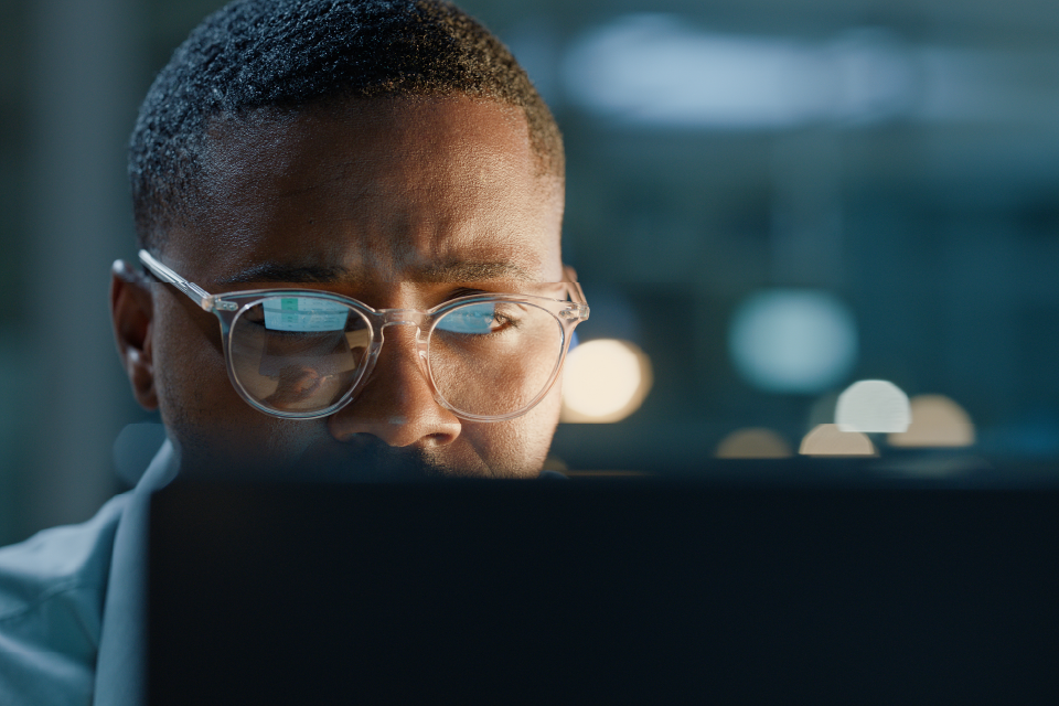A man in glasses is looking intently at a computer screen