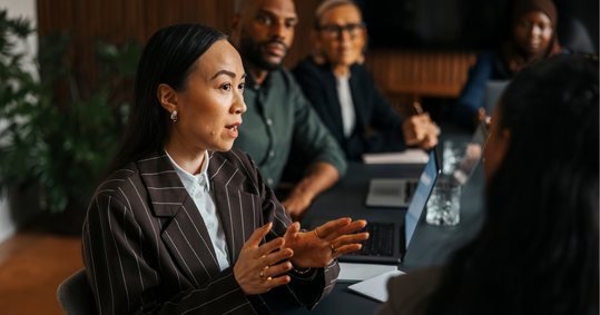 A woman in an office meeting  is talking as others look at her