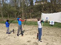 Three children taking part in archery in the countryside
