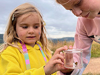 2 children looking at a butterfly in a collection pot