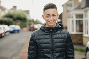 Teenage boy in black coat stands in street smiling at camera