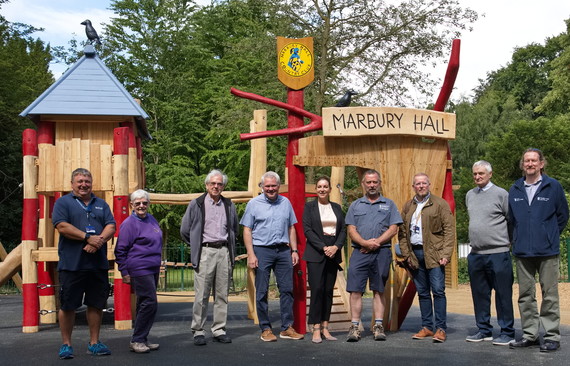 A group of adults stand in front of play equipment. 