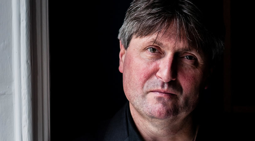 Man with dark hair looks at camera