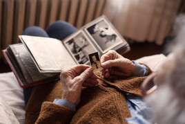 An older person seen from above looks through an album of sepia photos