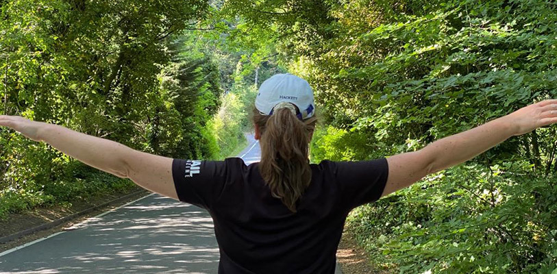 Woman in baseball hat with arms outstretched in woodland, viewed from behind 