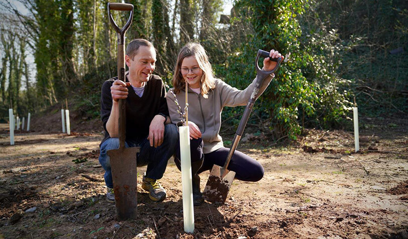 Man and girl kneel with spades, near saplings