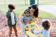 A mum and three children playing on a see-saw in the park