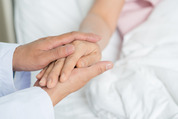 An elderly patient's hand being held, on a hospital bed
