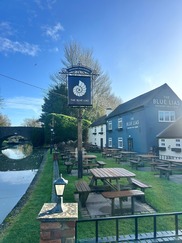 The Blue Lias pub sign with the building visible behind it alongside the river.